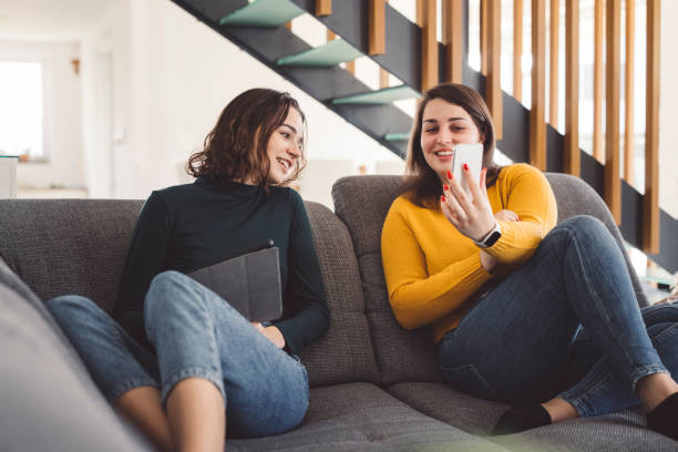 istock Sisters relaxing on the couch each with their own device 1287698910
