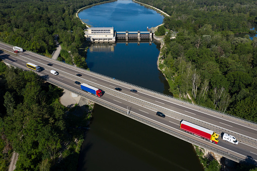 Heavy cargo on the highway bridge, and hydroelectric power station on Danube River, aerial view.