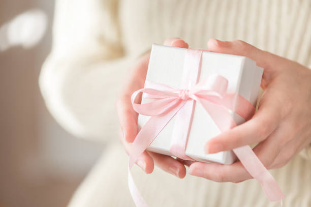 istock Female hands hold a white festive box with a pink bow. Gift for congratulations on birthday, Christmas, women's holiday. Winter cozy festive lifestyle. Surprise packaging 1287706406