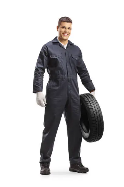 Smiling auto mechanic in a uniform holding a car tire isolated on white background