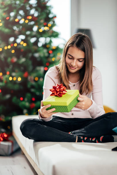 istock A cheerful girl opens a gift at the Christmas tree. 1287716900