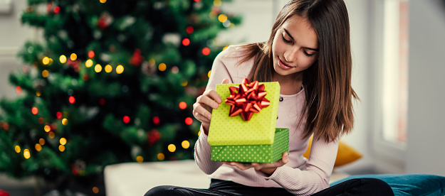 A cheerful girl opens a gift at the Christmas tree.