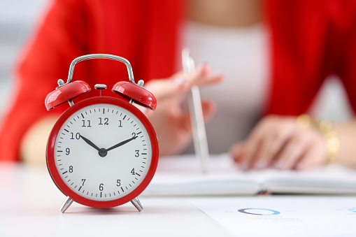 Against the background of businesswoman stands red alarm clock. Time management in business concept