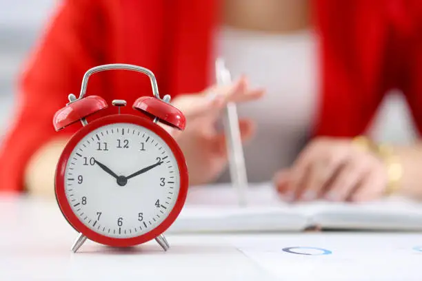 Photo of Against the background of businesswoman stands red alarm clock