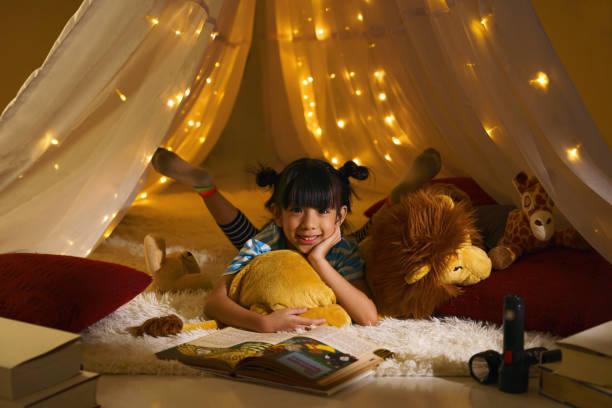 portret azjatyckiego dzieciaka bawiącego się w namiocie w salonie czytając bajkę. - child bedtime imagination dark zdjęcia i obrazy z banku zdjęć