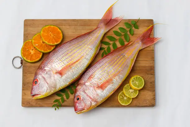 Top view of view of fresh Pink Perch (thread finned Bream) Decorated with lemon slice,Orange slice and curry leaves on a wooden pad,White Background,Selective focus.