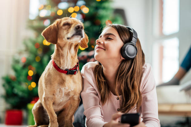 une adolescente écoute la musique tout en se trouvant sur l’étage avec son crabot près de l’arbre de noël - christmas tree audio photos et images de collection