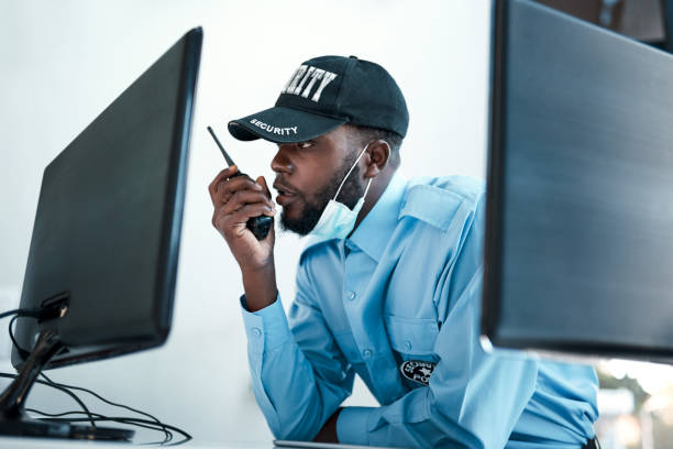 Your direct connection to first rate protection Shot of a young security guard using a two way radio while monitoring the cctv cameras security guard photos stock pictures, royalty-free photos & images