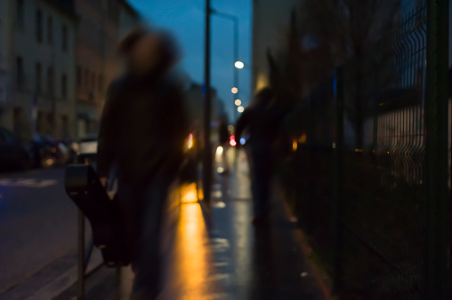 blurred silhouette of a man walking at night on the street carrying a musical instrument in his house