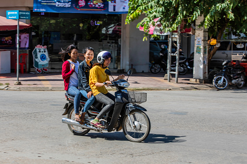 Three young Cambodian women having fun while riding a scooter through Battambang, Cambodia. Scooters are a common form of transport throughout Cambodia.