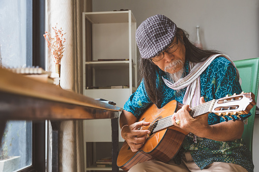 Asian senior men enjoy playing guitar in living room at home