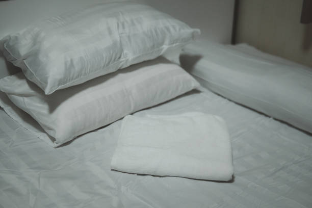 istock Close-up white bedding sheets and pillow with white towel. Fresh bed concept 1287769990