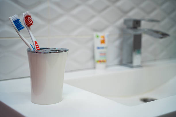 une paire de brosses à dents dans une tasse en plastique blanc sur un fond de tuiles blanches dans la salle de bains. les brosses à dents sont assises sur un évier en pierre blanche. - preserves jar empty red photos et images de collection