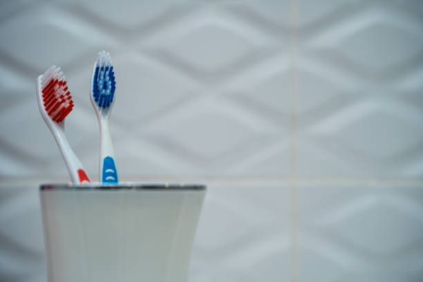 une paire de brosses à dents dans une tasse en plastique blanc sur un fond de tuiles blanches dans la salle de bains. - preserves jar empty red photos et images de collection