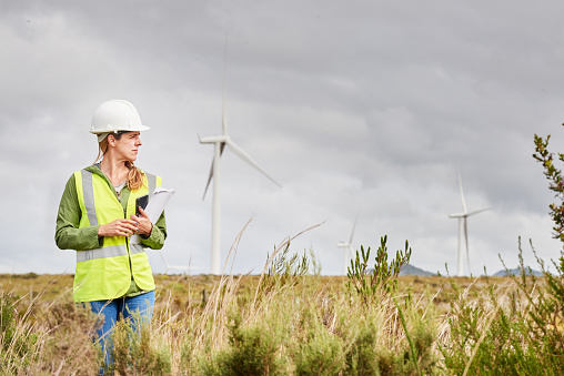 Young female engineer working in a field with wind turbines in the background on an overcast day