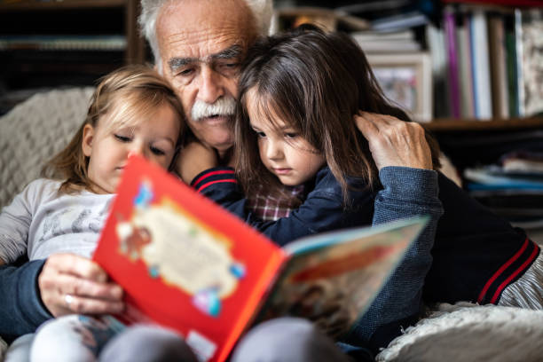 Adorable little girls reading kids book with Grandpa stock photo