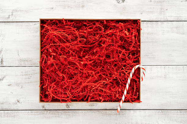 Opened gift box with red shredded paper on white wooden background. Flat lay, top view. Box for your product replacement. Xmas.