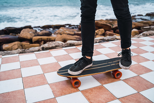 Portrait of young man practising his tricks on the skateboard with sea at the background. Sport concept.