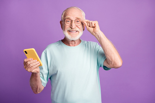 Retrato fotográfico del hombre feliz tocando gafas sosteniendo el teléfono en una mano aislado en el fondo de color violeta vivo photo