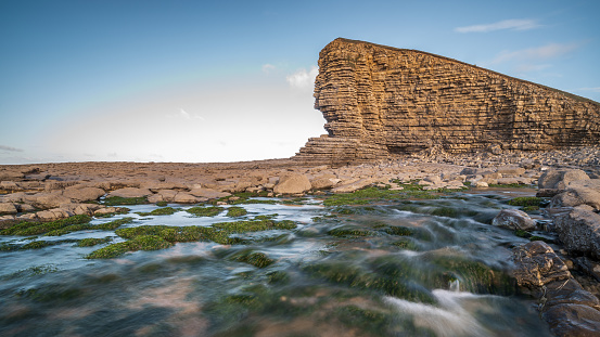 Large geological feature at Nash Point, south Wales, with a stream of water running beneath the cliff face