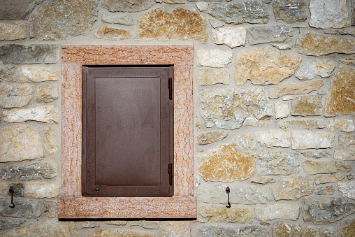 Closeup of a rustic stone house with a window with closed metal shutter, Lessinia Plateau, Italian Alps, Veneto, Verona province, Italy, Europe.