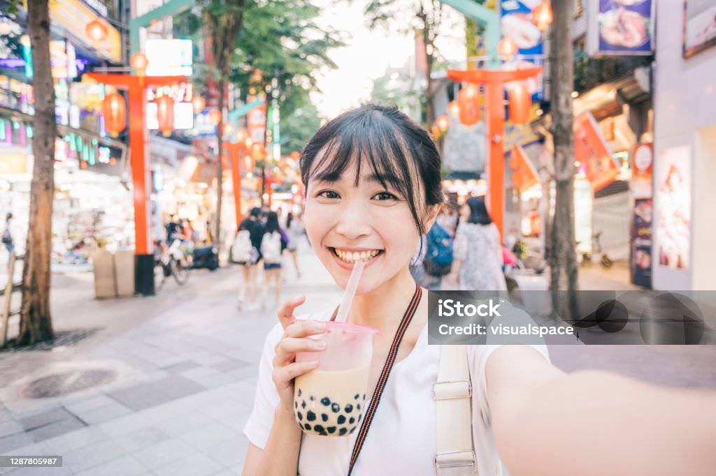 Young Asian woman taking a selfie Point of view image of Taiwanese woman taking a selfie. She's looking at the camera, drinking bubble tea. Influencer Stock Photo