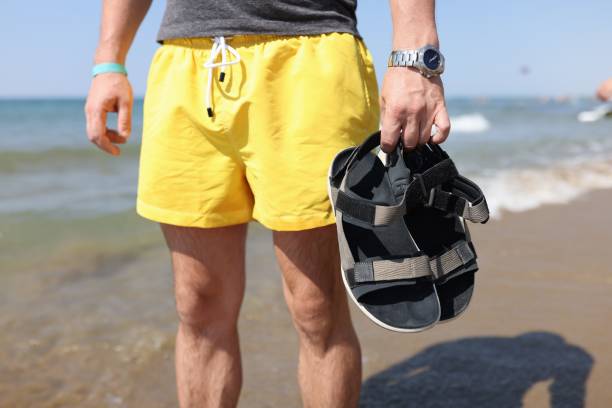 l’homme se tient dans un t-shirt et des shorts dans ses mains retenant ses chaussures sur le fond de la mer. - manche de qualification photos et images de collection
