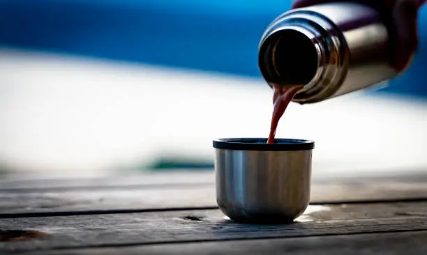 Photo of Hiker pouring a hot drink from a metal thermos bottle into a steel mug.