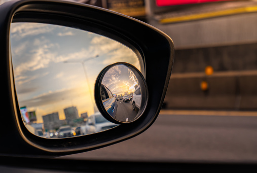 Reflejo del flujo de tráfico en carretera asfáltica en espejo lateral de SUV azul. Espejo de ala de coche con espejo convexo para la conducción de seguridad. Vista en la carretera y el cielo de la puesta de sol detrás del paisaje urbano a través del e photo
