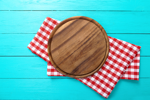 Frame of round cutting board and red plaid tablecloth. Blue wooden background in the restaurant. Copy space
