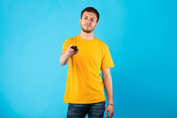 Man holding remote control isolated on blue background Portrait of man holding remote control in hand, pointing it against camera, watching tv, changing channels, standing at studio, isolated over blue background. Relaxation And Rest Concept control point stock pictures, royalty-free photos & images