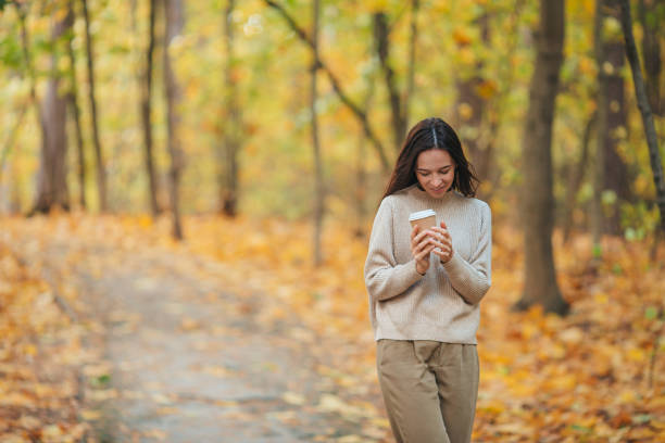 istock Fall concept - beautiful woman drinking coffee in autumn park under fall foliage 1287823929