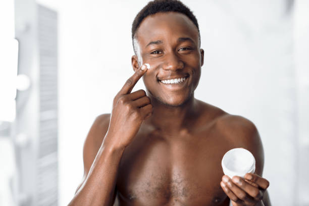 istock Black Man Applying Cream On Face Standing In Bathroom Indoors 1287825133