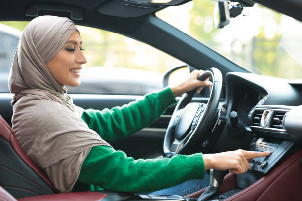 istock Cheerful muslim woman driving car, using dashboard 1287825401