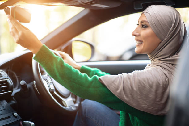 バックミラーを調整する一人で運転する幸せなイスラム教徒の女性 - owner women car rear view mirror ストックフォトと画像