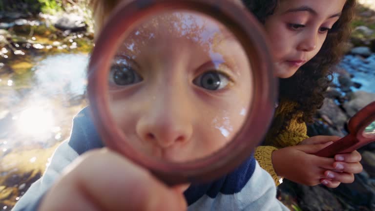 Small boy and girl looking at camera with magnifying glass