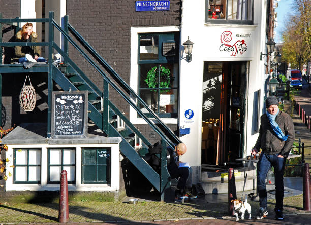 On a bright and cold autumn afternoon, a man walks with his dog by the Prinsengracht in Amsterdam one of the landmarks of the city. Two people sitting by themselves on an outdoor staircase, seem undisturbed while taking this wonderful moment to read or just relax.