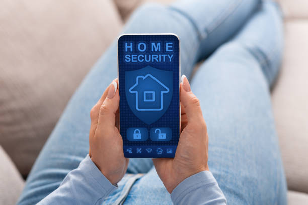 Woman using her smartphone with home security application Smart house, home automation, device with app icons. Over the shoulder view of woman using her smartphone with home security application on the screen to unlock the door of the house burglar alarm stock pictures, royalty-free photos & images
