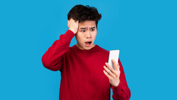 istock Surprised shocked asian man using mobile phone on blue wall 1287831082