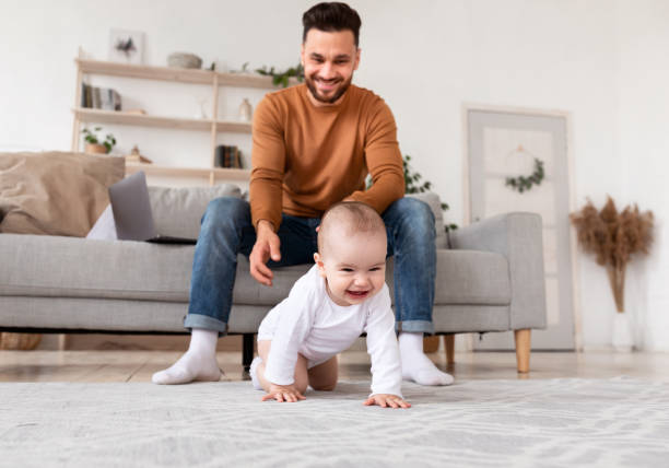 istock Happy Daddy Looking At Baby Crawling On Floor At Home 1287831970