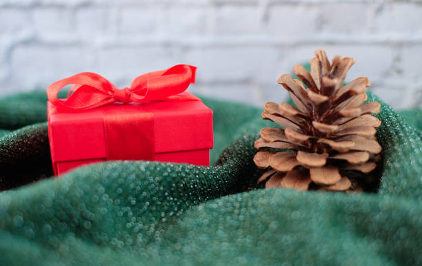 istock Christmas and new year composition - pine cone, and red gift box on green knitted sweater with brick wall background 1287832431