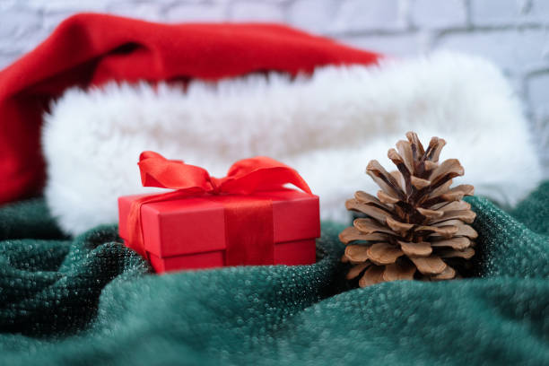 istock Christmas and new year composition - pine cone, red gift box and santa hat on green knitted sweater with brick wall background 1287832477