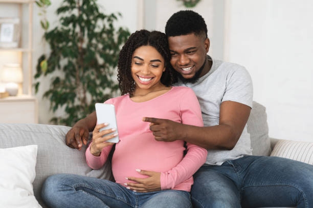 istock Happy pregnant black couple using smartphone together at home 1287835771