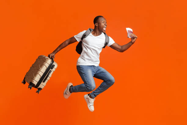 istock Happy black man with passport and suitcase jumping up 1287836027