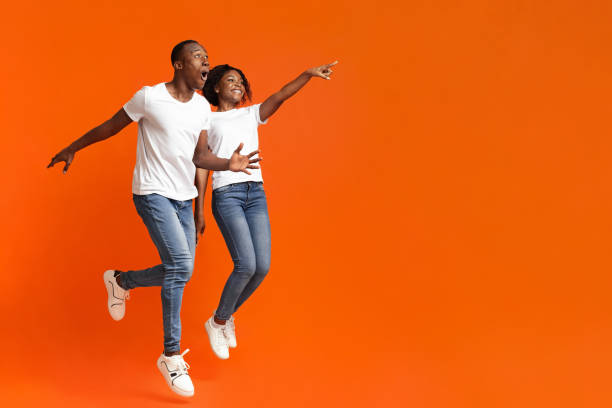 istock Emotional black man and woman jumping, pointing at empty space 1287836343