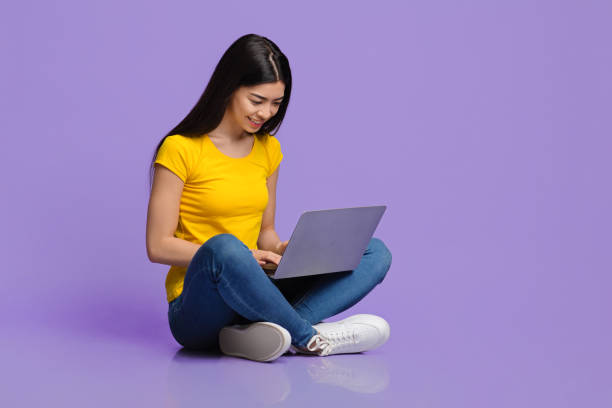 concetto di lavori online. giovane donna coreana sorridente seduta sul pavimento usando il laptop - floor sitting foto e immagini stock