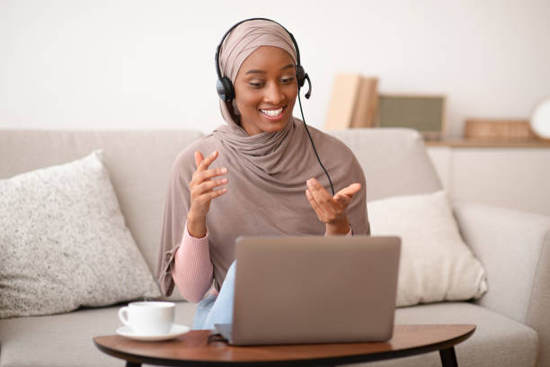 lavoro online, comunicazione, istruzione. donna musulmana nera in hijab con videochiamata su laptop a casa - east asian ethnicity foto e immagini stock