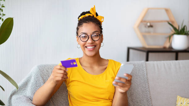 집에서 스마트 폰과 신용 카드를 들고 있는 흑인 여성 - black friday 뉴스 사진 이미지