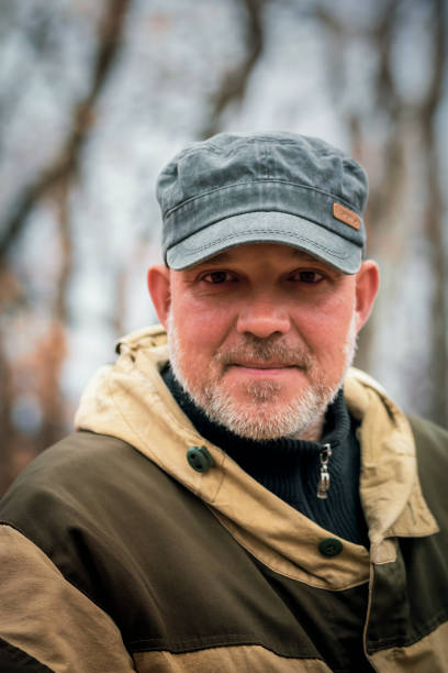 야구 모자를 쓰고 40~45세의 웃는 남자의 초상화와 자연의 숲을 배경으로 가을에 야외 활동을 위한 따뜻한 위장 계절 아우터웨어 - 40 45 years 이미지 뉴스 사진 이미지
