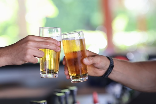 Two male hand hold glass of cold beer and clink glasses. Spending time in male company in bar.